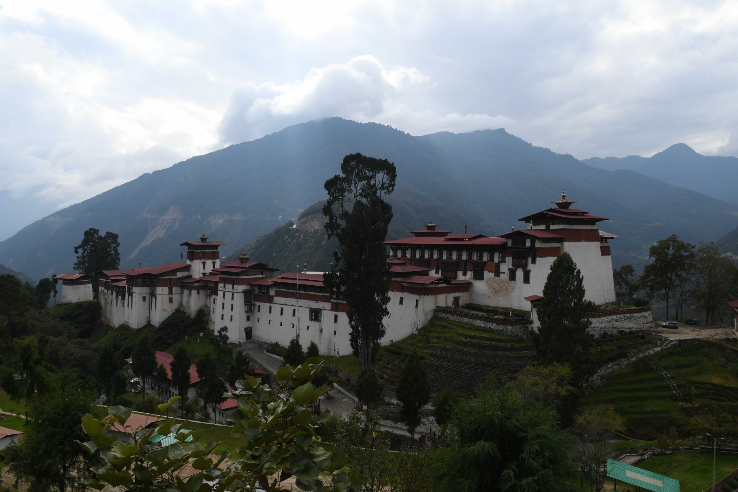 A hilltop dzong with red roofs below cloud-covered mountains