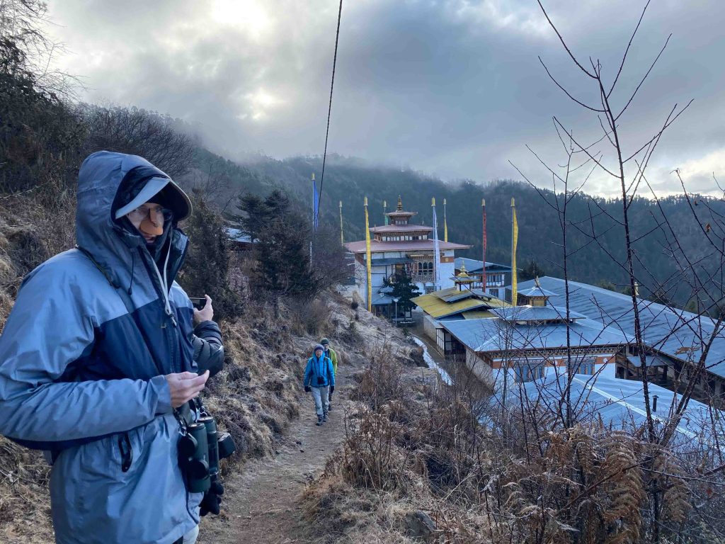 A birder with binoculars on a misty trail above a monastery in Bhutan