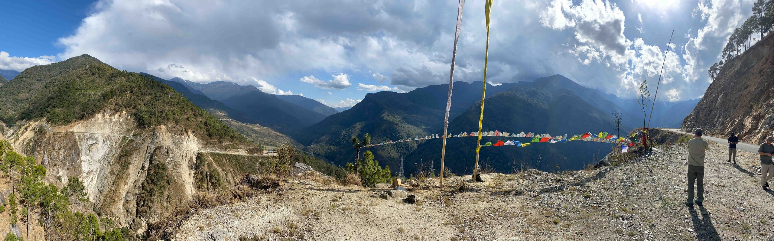 Prayer flags strung above a roadside viewpoint, Himalayan ridges receding into haze beyond