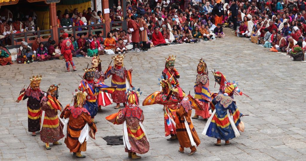 Masked dancers circling a festival courtyard as crowds look on