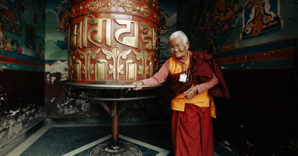 An elderly woman turning a large prayer wheel inside a Bhutanese temple